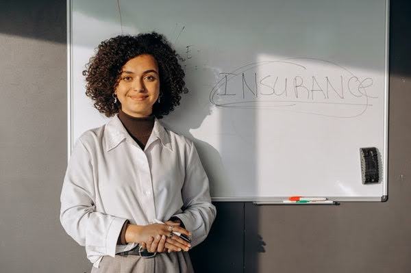 A woman standing next to a white board with the word insurance written on it