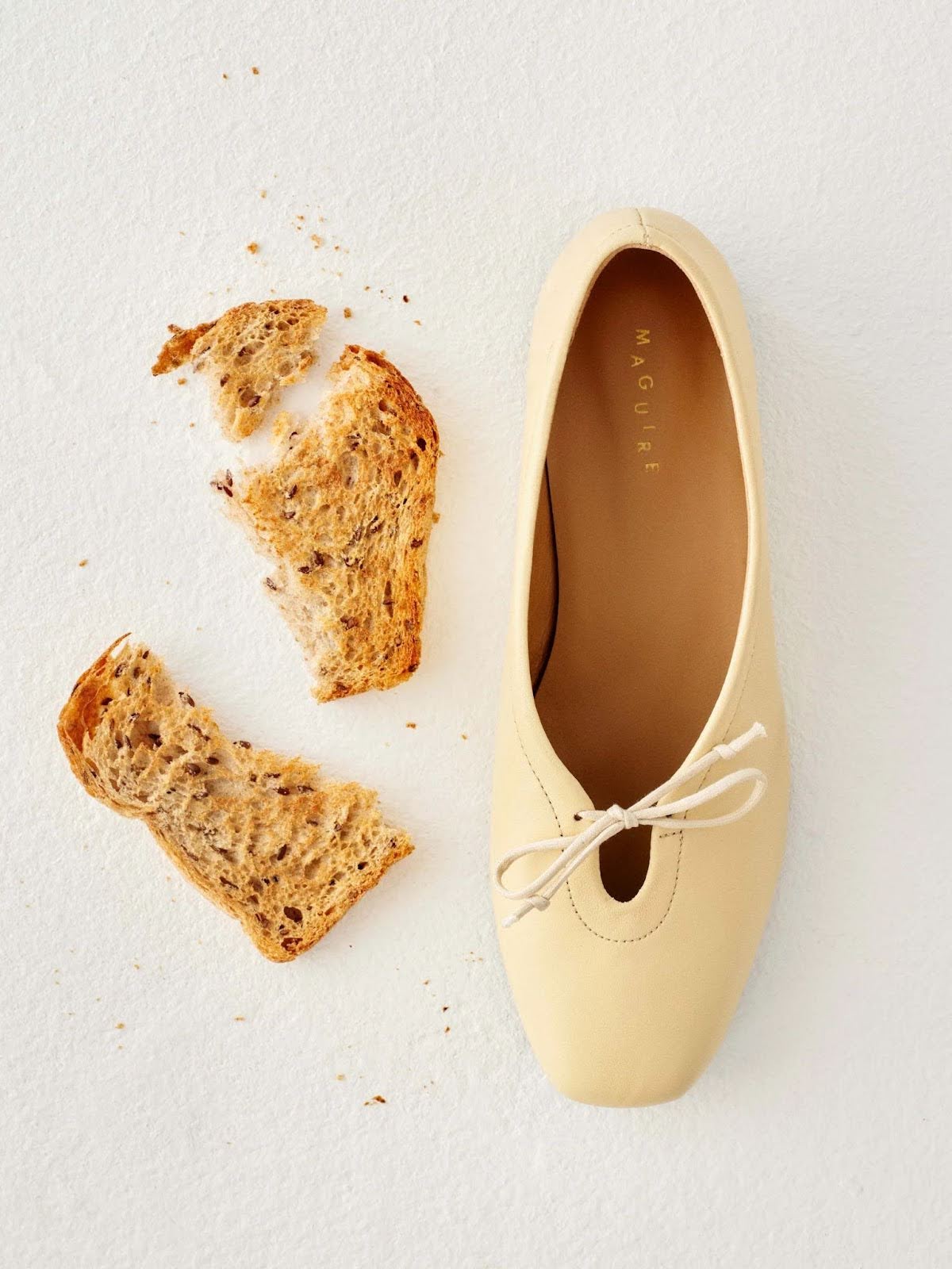 A butter-yellow ballet flat photographed from overhead beside a piece of toast.