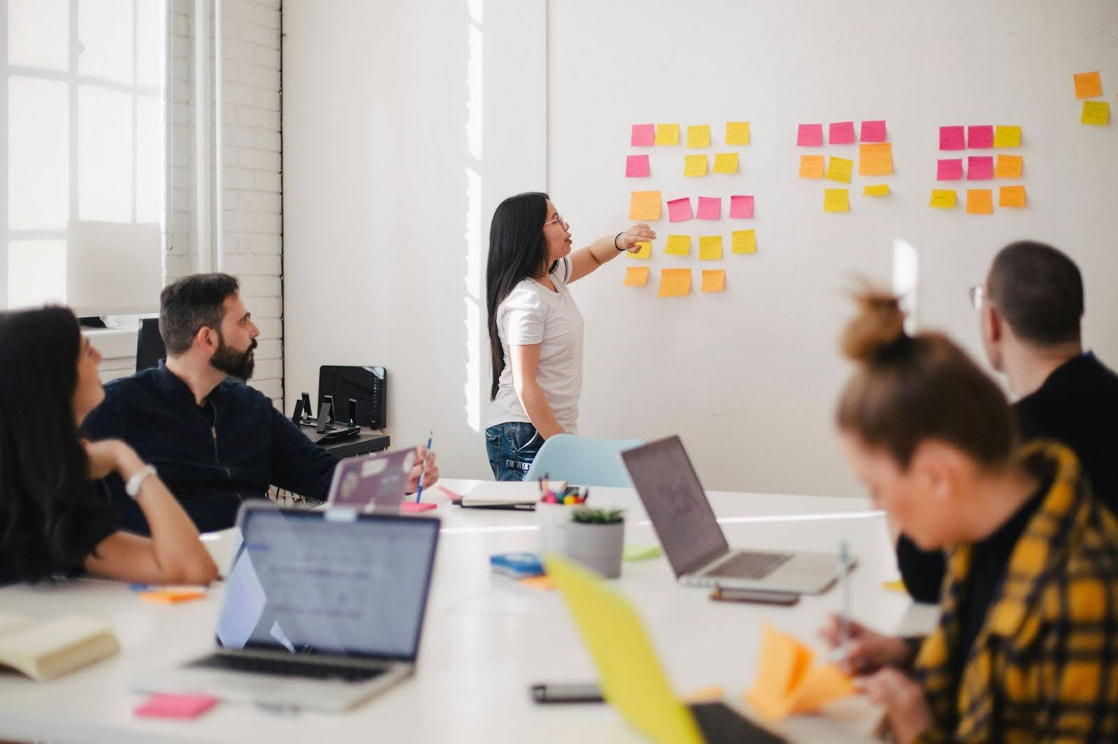 People in a boardroom brainstorming business ideas with sticky notes on a whiteboard.