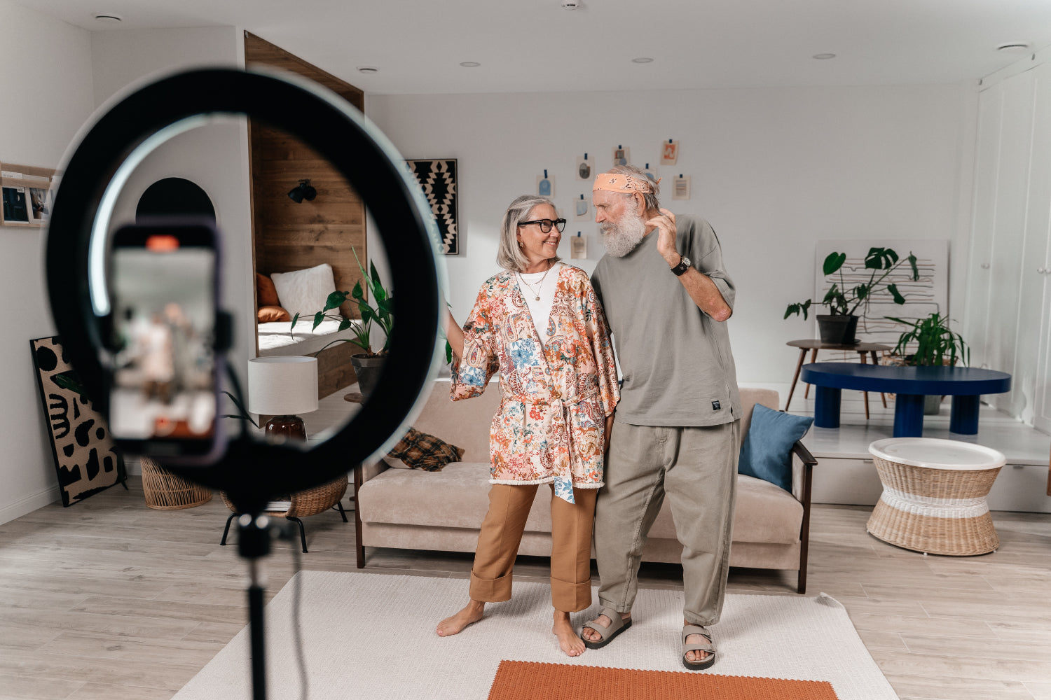 An older couple shoots a video of themselves in a living room