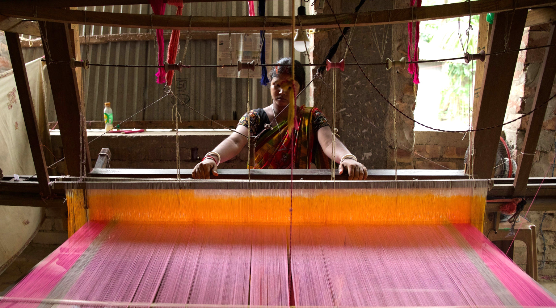 An artisan using a weaving machine to create a pink and gray fabric. 