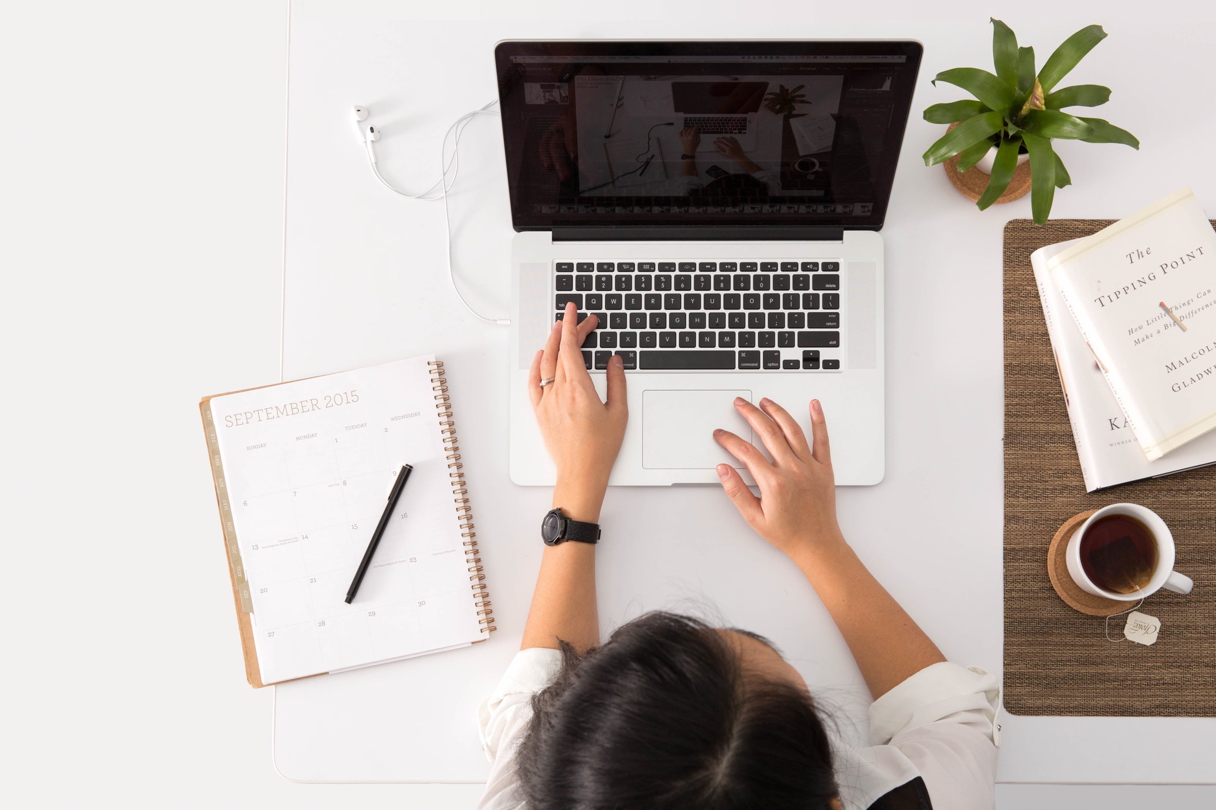 Person photographed from above working on a laptop covered in office supplies