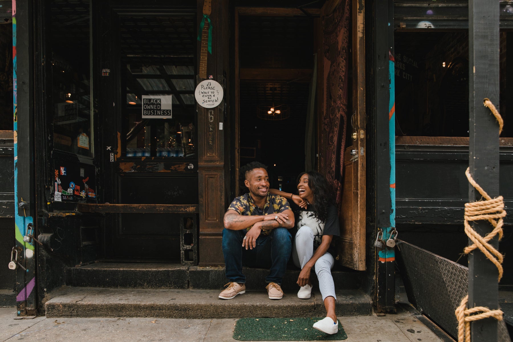 A couple sits on the stoop in front of a small retail business