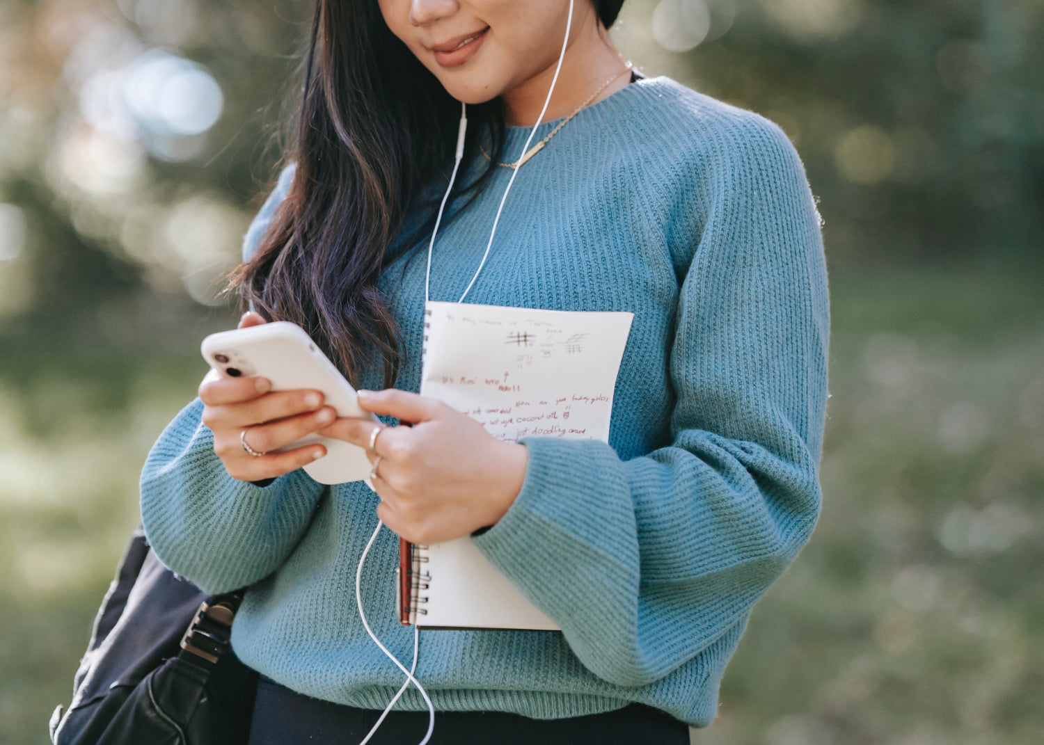 A woman types on a mobile phone while standing outside and wearing headphones