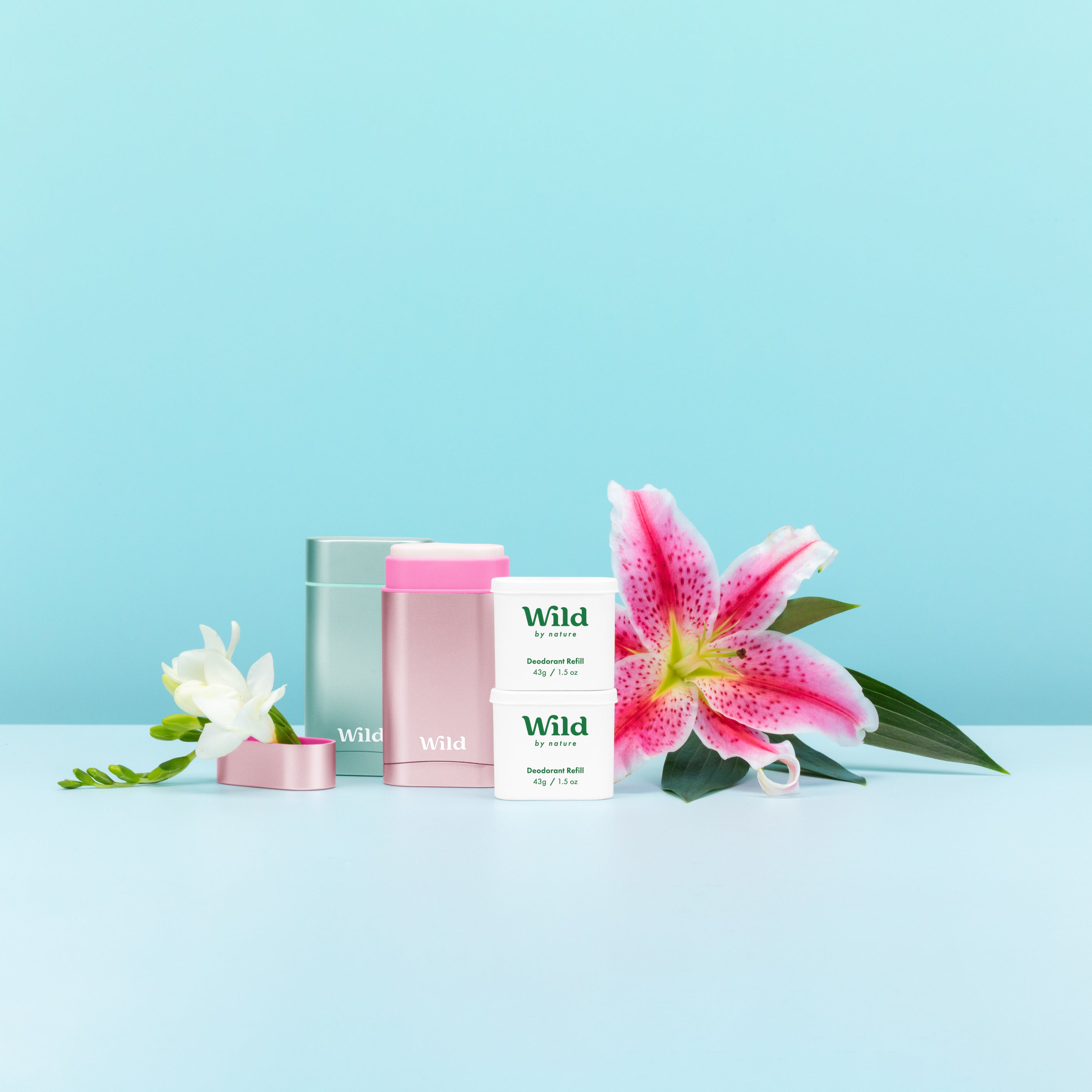 2 Wild aluminum deodorant cases and 2 refills near a large pink orchid flower against a blue background. 