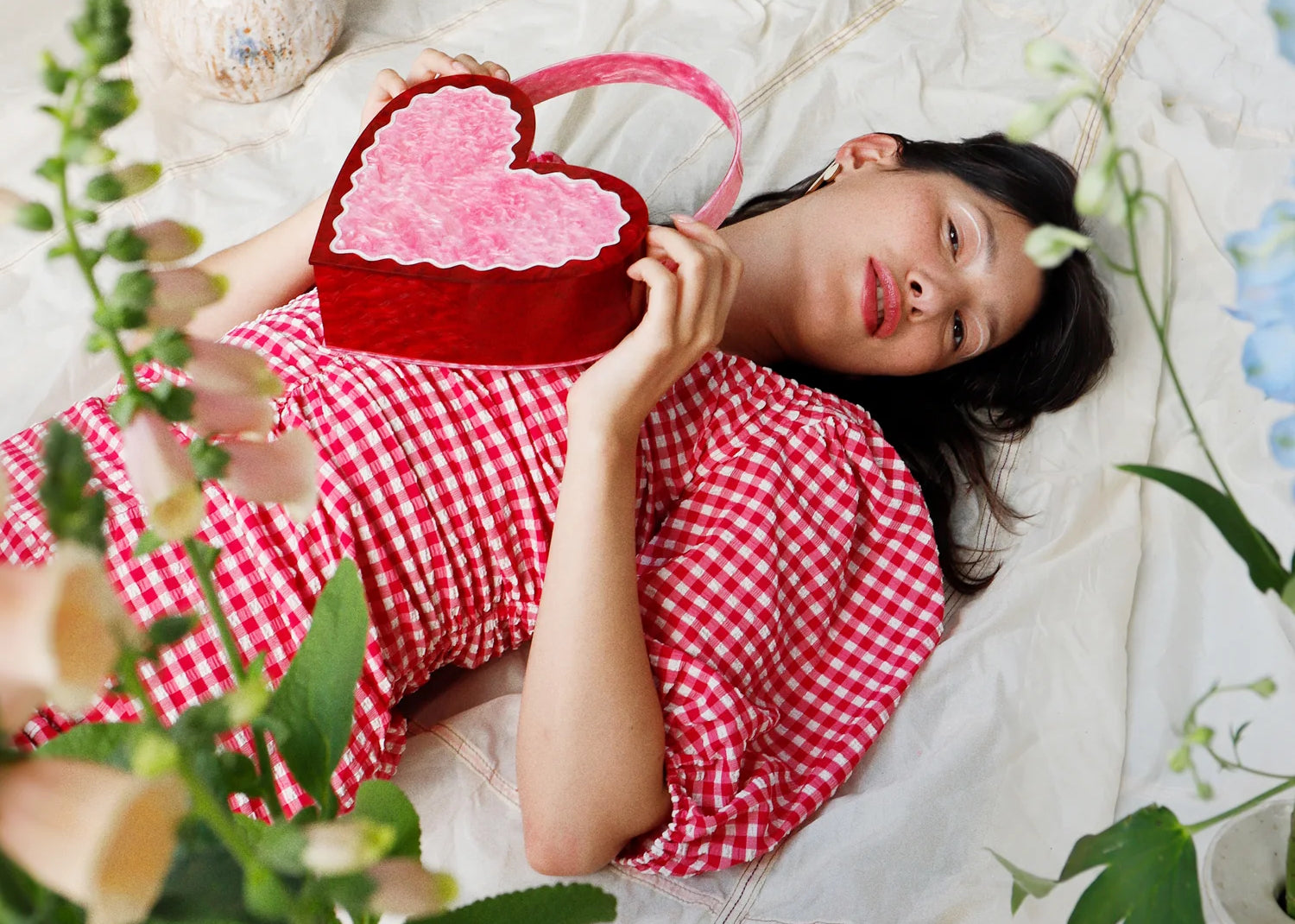 A woman in a red gingham dress lies on the floor holding a heart shaped purse