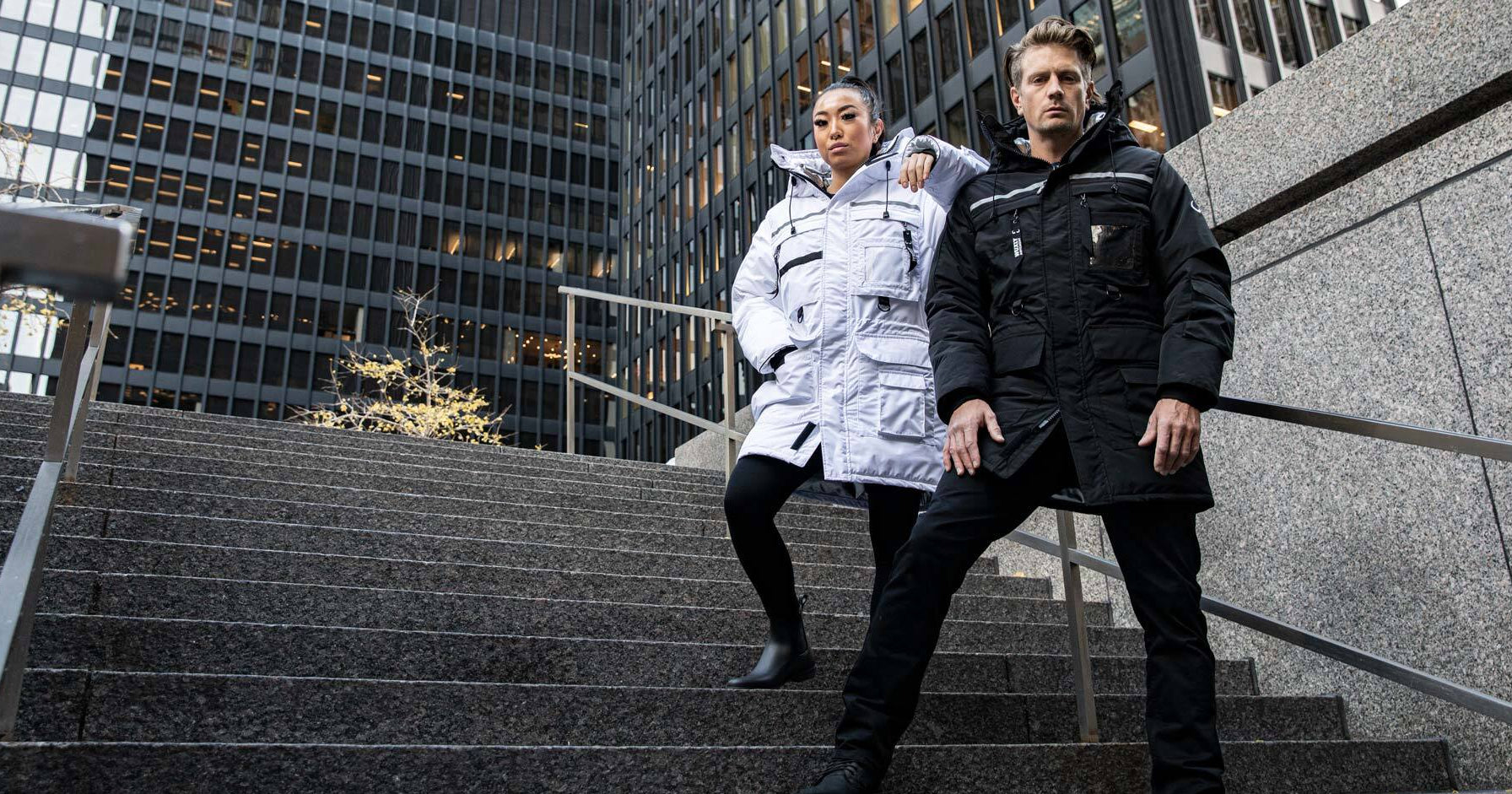 Two people in winter coats stand on cement steps outdoors