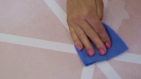 A ladies hand with pink nail varnish cleaning milk from a Toddlekind Vintage Nude pink playmat