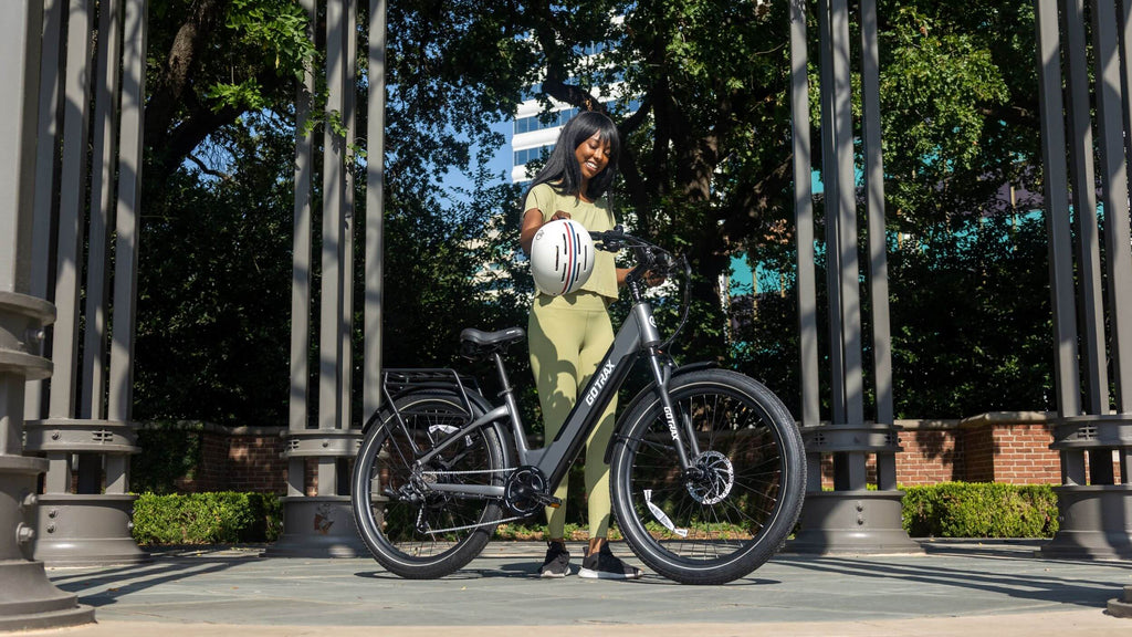 A woman standing with the GOTRAX CTI 3 electric bike with a rear storage rack and removable battery.