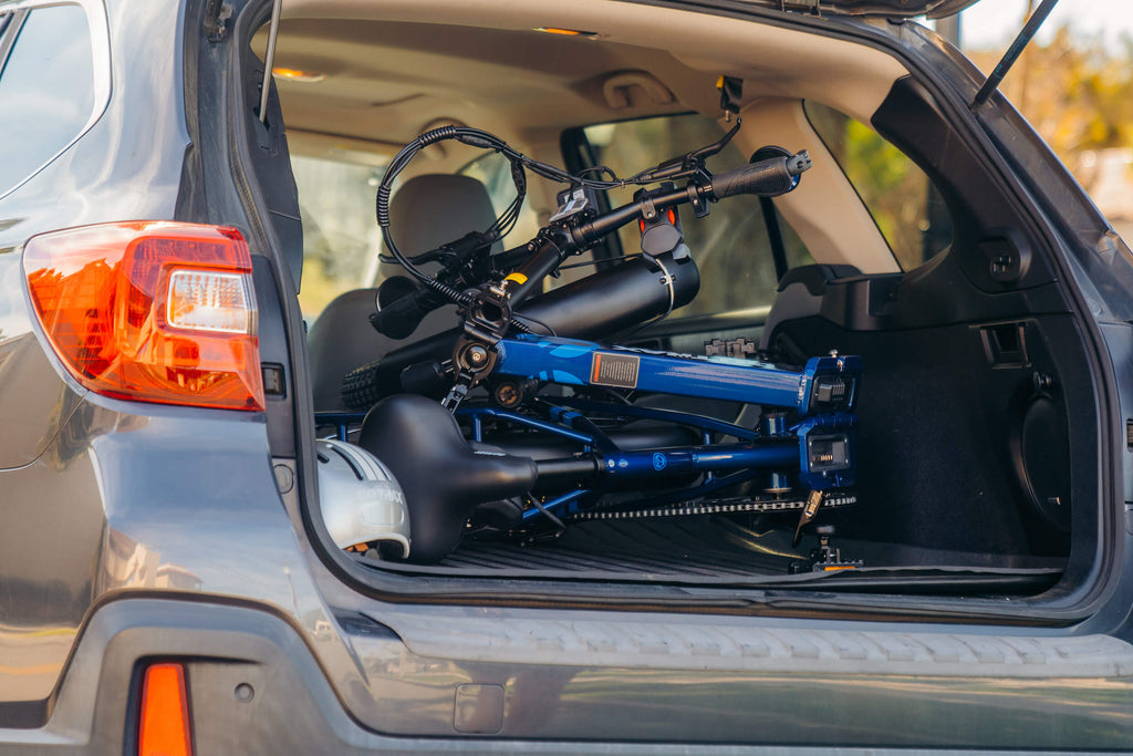 The GOTRAX F2 V2 folding electric bike with hydraulic brakes folded up and stored in the trunk of a car.