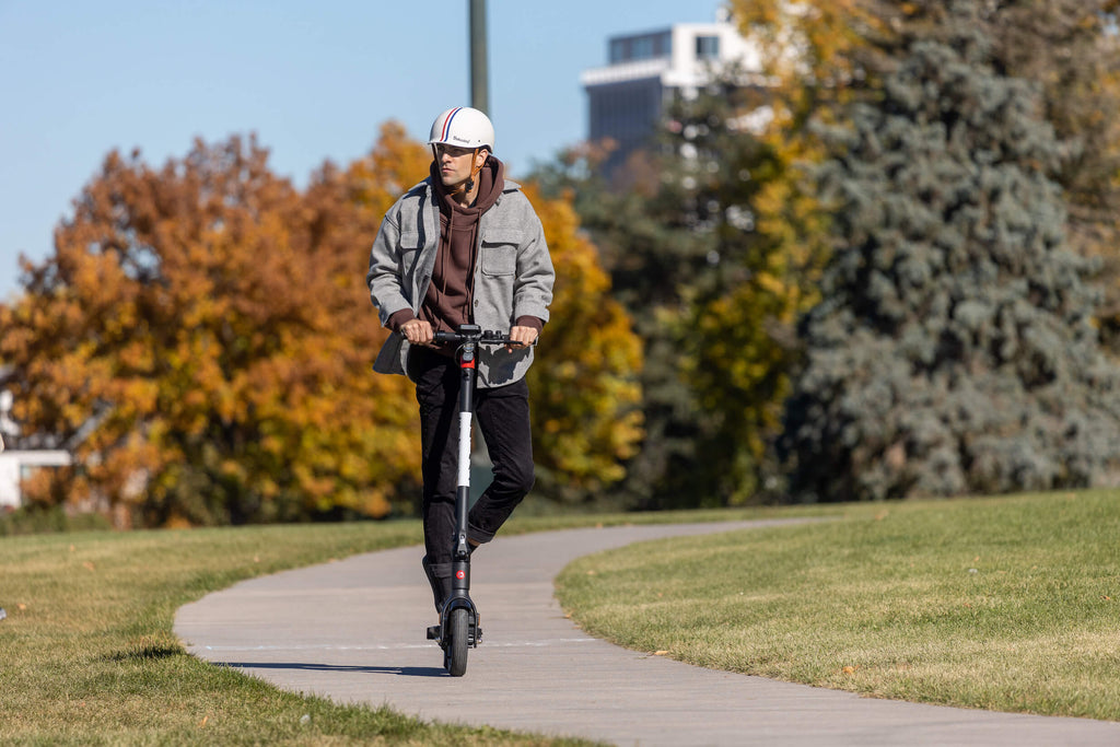 A man riding the GOTRAX G4 folding electric scooter for adults on a paved path.