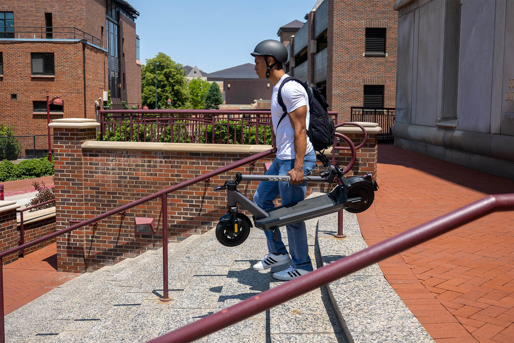 A young man carrying the GOTRAX G6 foldable commuter electric scooter with 10" tires down a set of stairs.