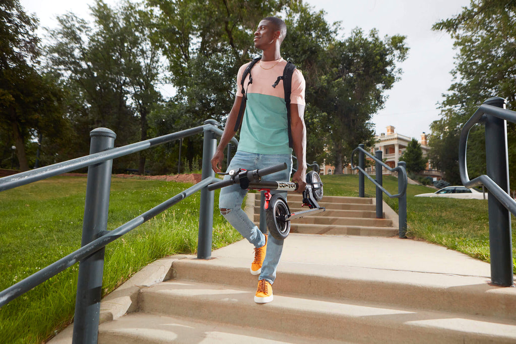 A man carrying the GOTRAX GXL V2 electric scooter with a 250 watt motor and folding frame down a set of stairs.