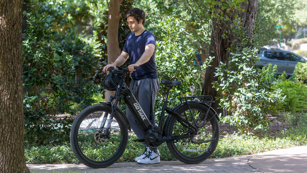 A man walking the new GOTRAX MX1 Mid-Drive Electric Bike with wide 3" tires and a rear cargo rack.