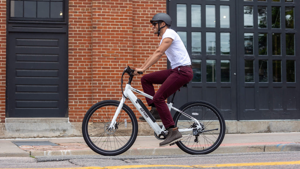 A man riding the GOTRAX CTI Electric Bike with a removable battery and multiple frame options down a city street.