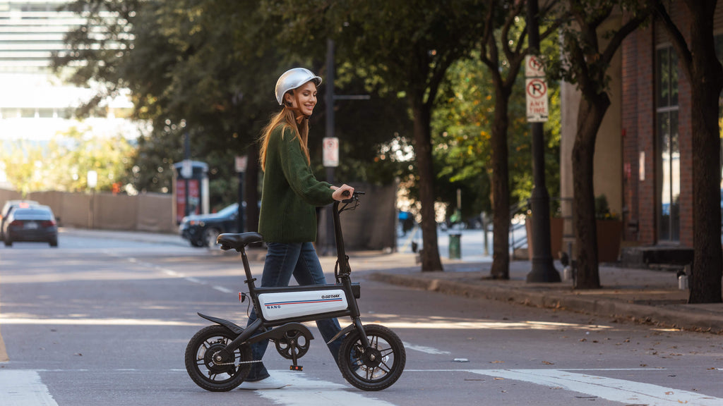 A woman walking the GOTRAX Shift S2 Nano compact electric bike with folding handlebars down a street.