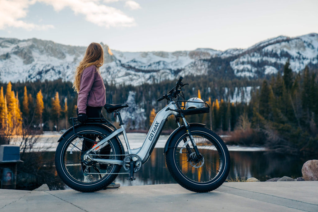 A woman standing by a lake with a GOTRAX Tundra all-terrain fat tire ebike.
