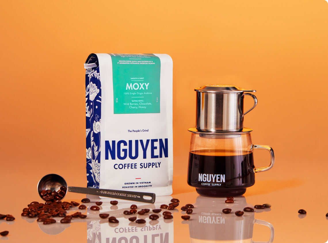 Nguyen Coffee Supply bag, brewing device, coffee cup, and scattered coffee beans on orange background.