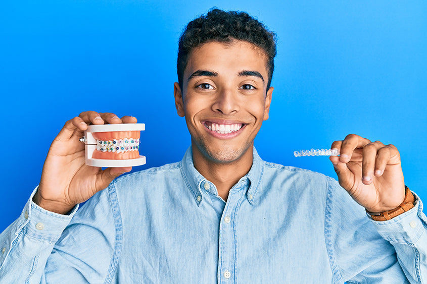 a smiling man holding a model of teeth with braces and an invisible aligner