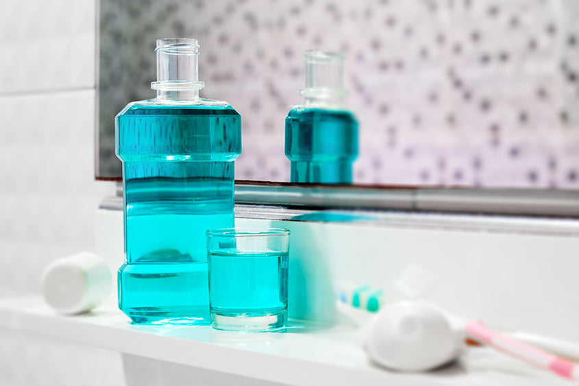a bottle and a small glass of mouthwash on a small shelf in a bathroom