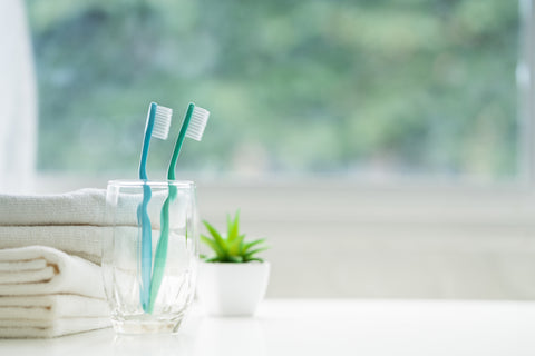 toothbrushes in a glass and white towels on white counter