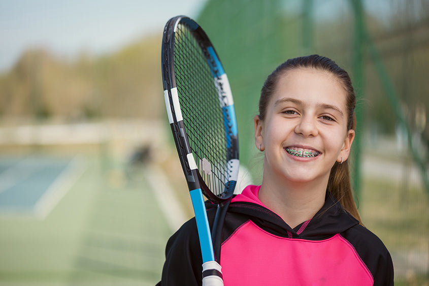 a smiling girl with braces holding a tennis racket