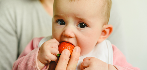 unhappy baby eating a strawberry 