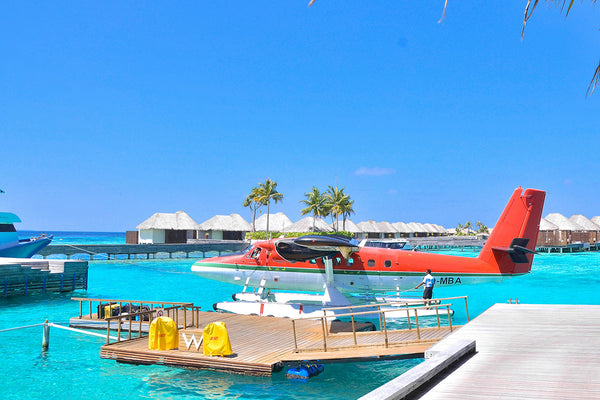 a small red water plane sits on the teal water under a clear blue sky