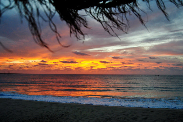 a burnt orange sunset illuminates a cloudy sky with rolling waves into the beach