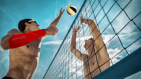 Two men reach for a volleyball over a net; one of them is wearing an eSmartr smart compression sleeve in the POWER style.