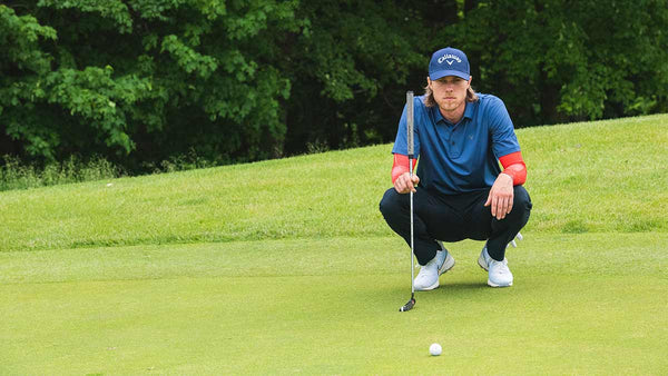 Professional golfer Adam Migur intently analyzes a golf ball before he makes his next shot.