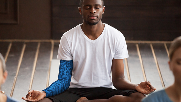 A young man meditates in a class with friends, an eSmartr smart compression sleeve on his arm.