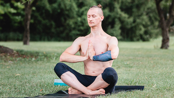 A young man meditates in a park with an eSmartr sleeve on his arm.