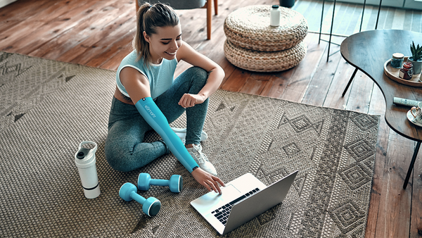 A young woman pauses her exercise routine, an effective way to combat stress and anxiety, with an eSmartr sleeve on her arm.