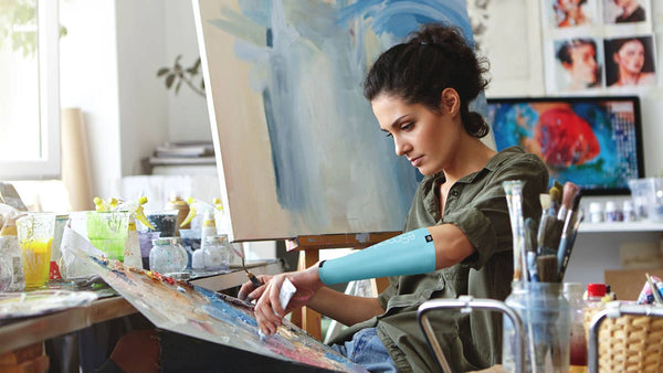 A woman paints in her studio, with a smart compression sleeve on her arm for mental calmness.