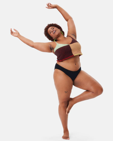 A Black woman wearing a knit crop top and black cotton leakproof lace underwear dances for the camera