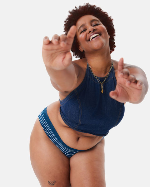 A Black woman wearing a denim halter top and Kt by Knix period underwear dances
