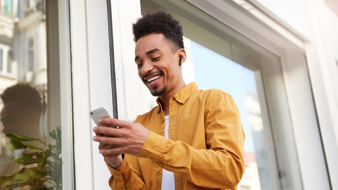 Young Man Happily using Morpheus 360 TW2750B Wireless Earbuds While Scrolling Through Mobile Phone_16 to 9 Frame