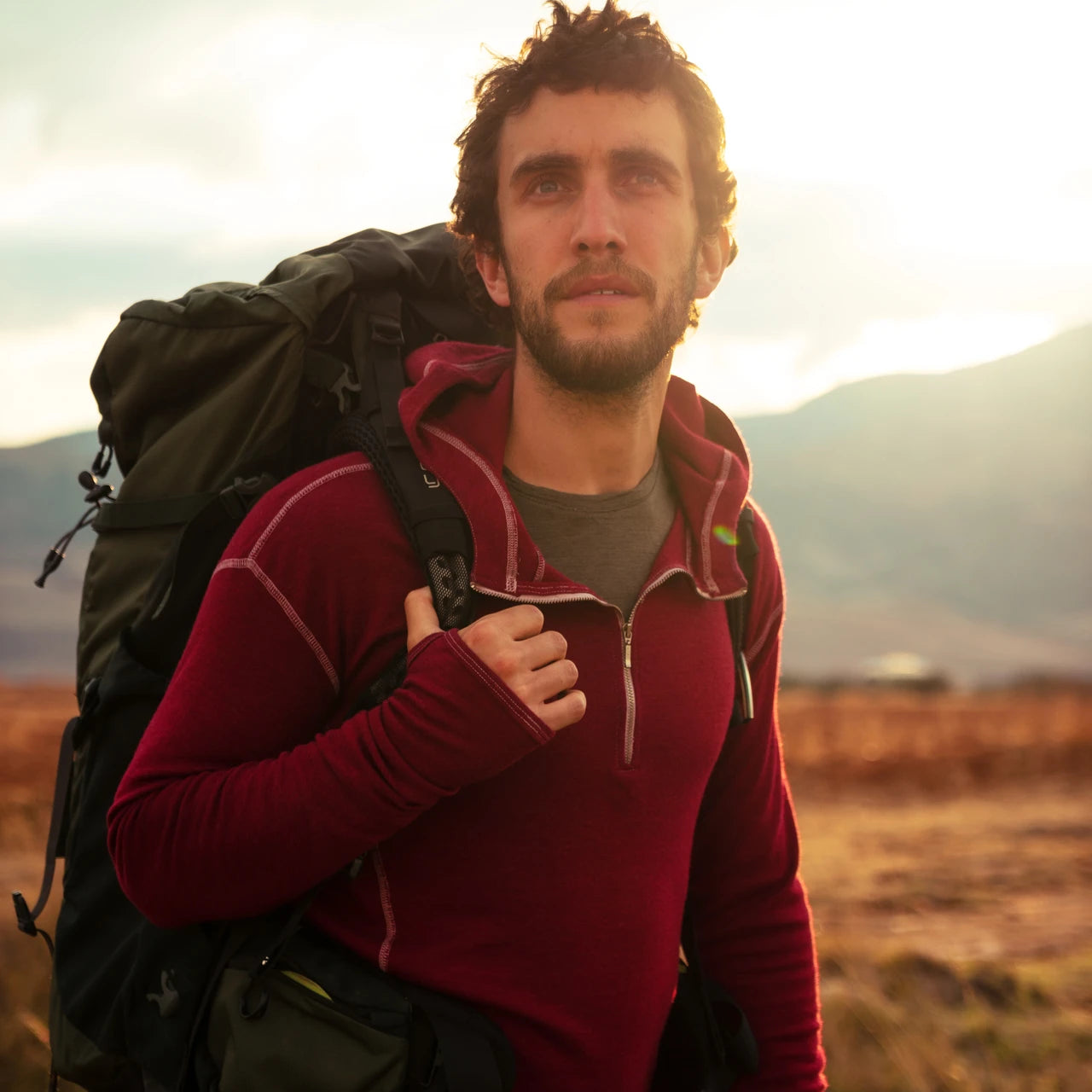 A man hiking in the mountains with a backpack wearing alpaca wool hoodie