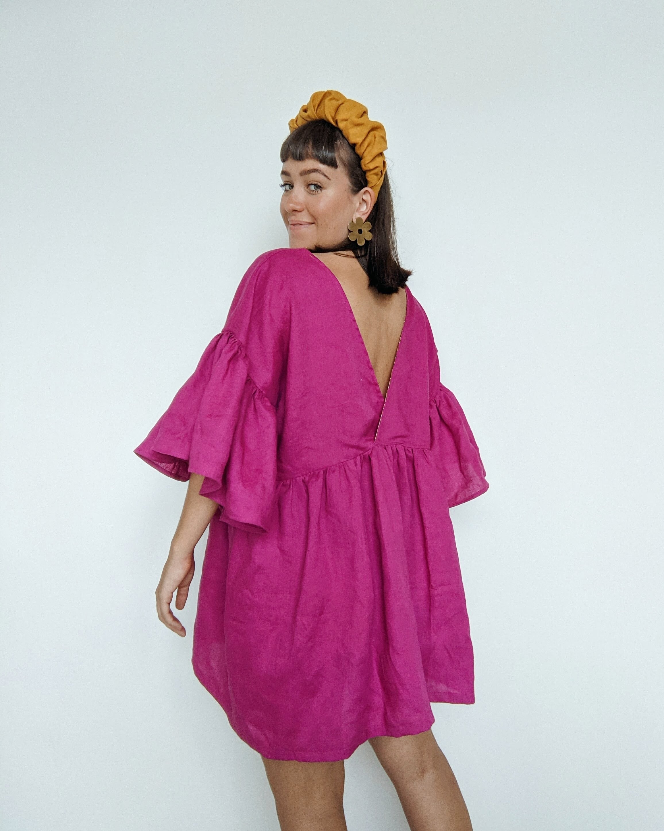 Daisy stands with her back facing to show the v back on her magenta linen Maya ruffle dress hack.