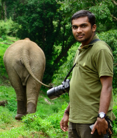 Photographer from the Elephant Family NGO with an elephant walking away in the background of a jungle