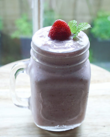 Light pink strawberry smoothie in mason jar with strawberry and mint garnish on top