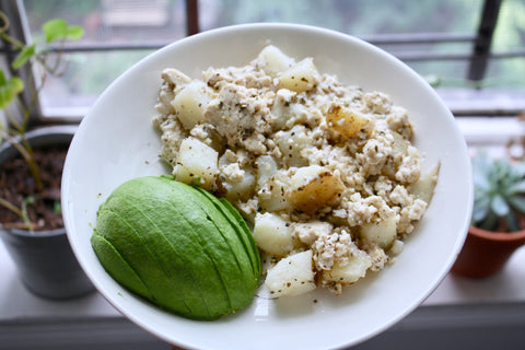 Vegan tofu scramble with half an avocado on a white plate by a sunlit window