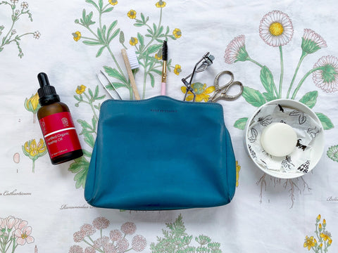 Small blue purse with beauty products spilling out. Laid out on floral cloth.