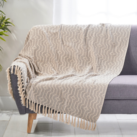 A boho blanket draped over a gray sofa