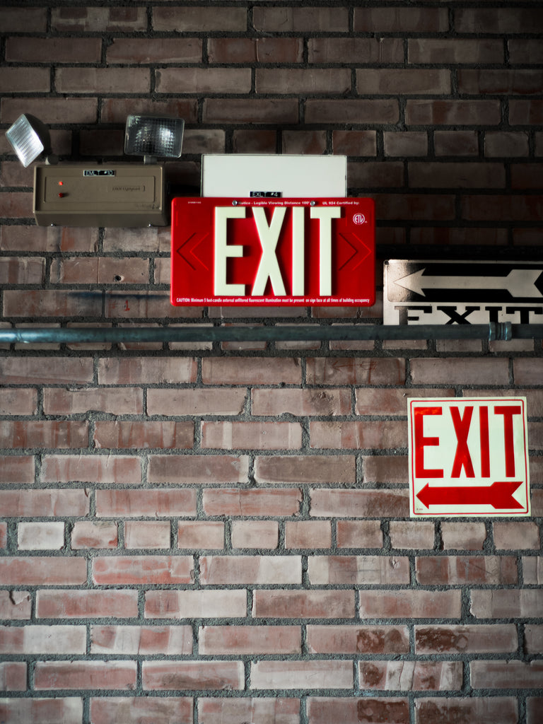 Multiple exit signs plastered on a brick wall.