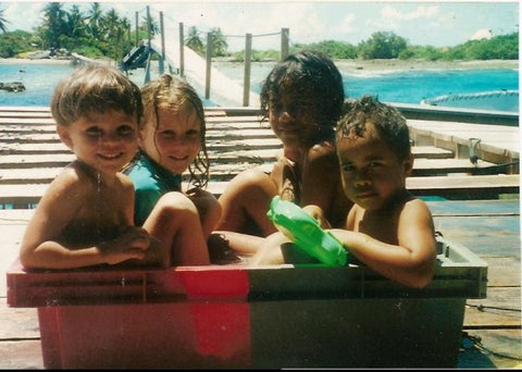 Four kids sit together in an oyster tub. The bridge to the farm over a bright blue lagoon is visible in the background.