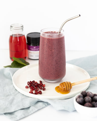 Healthy purple smoothie on white table surrounded by ingredients and Manuka Honey