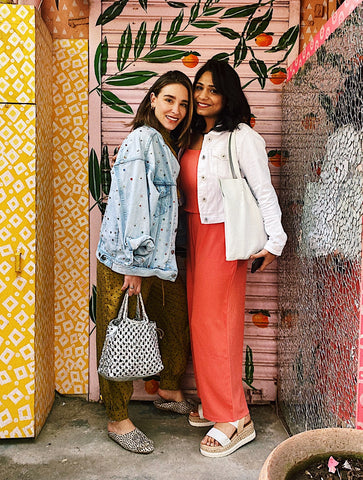 two women wearing bright colors in from of a wallpapered wall