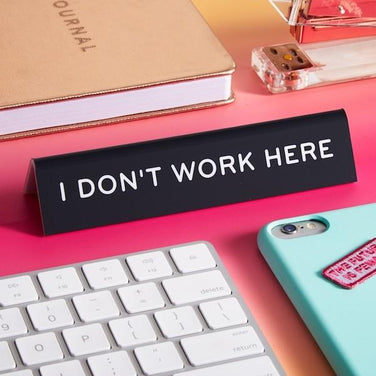 https://cdn.shopify.com/s/files/1/0072/1432/products/the-found-office-goods-desk-sign-i-don-t-work-here-funny-gag-gifts-21097668280481.jpg?v=1628407378&width=376